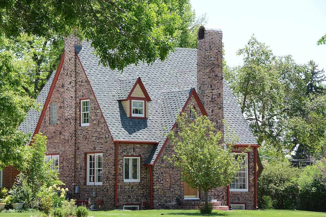 A 1920s brick house with a tile-capped chimney under mature trees